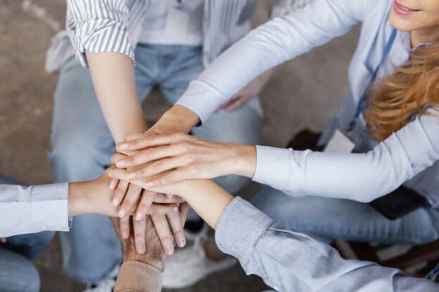 Five people forming a circle, hands clasped together, symbolizing unity and teamwork.