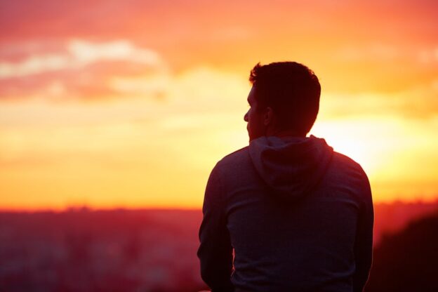 A man sitting on a hill, gazing at the sunset during Adolescent Group Therapy for Social Skills.